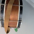 Valcový buben s dřevěným korpusem v hnědé barvě a černými okraji. Nástroj má kovové obruče a je přes něj přeházena hnědá textilní popruhová páska. Po…