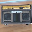 Hnědý akustický zesilovač s kovovými rohy a černou ochrannou mřížkou před dvěma reproduktory. Na horním ovládacím panelu je nápis AC75 a logo ACOUSTI…
