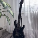Černá elektrická kytara s černým hmatníkem a černým hardwarem, umístěná na stojanu. Na hlavě kytary je bílý nápis "Washburn". Tělo i krk jsou v leskl…
