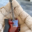 Elektrická kytara s červeným gradientem, dvojcutem a hnědým hmatníkem. Na hlavě je bílý nápis Gibson. Nástroj má dva humbuckery, tři ovládací knoflík…