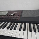 Detailní pohled na ovládací panel a klávesnici elektronického klavíru v černé a hnědé barvě. Na panelu jsou vidět tlačítka, displej a ovládací knoflí…