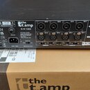Černý výkonový zesilovač s nápisem the t.amp E4-130. Zadní panel obsahuje čtyři výstupy OUTPUT (CH-1 až CH-4) a čtyři vstupy INPUT (CH-1 až CH-4), do…