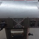 Zadní strana šedého elektronického zařízení s kovovým šasi a ventilačním ventilátorem uprostřed. Vpravo jsou vstupy a výstupy s popisky LINE OUT, INP…