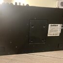 Fotografie zachycuje spodní stranu černého elektronického zařízení s matným povrchem. Na spodní části je umístěn bílý štítek s varovnými texty, logy…