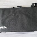 Černý textilní obal na hudební nástroj s rukojetí a ramenním popruhem. V levém dolním rohu je bílý nápis YAMAHA s doprovodným logem značky. Povrch ma…