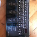 Šedý multifunkční efektový pedál Boss ME-80 Guitar Multiple Effects. Zařízení obsahuje čtyři černé spínače, několik otočných potenciometrů a digitáln…