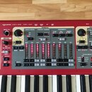 Červený digitální klavír s bílo-černými klávesami. Ovládací panel obsahuje sekce ORGAN a PIANO s různými přepínači, posuvníky a tlačítky. Jsou zde ná…