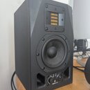 Černý studiový monitor v hranaté skříni. V horní části je umístěn páskový výšek s žlutým membránovým prvkem, uprostřed je kruhový střední reproduktor…