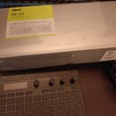 Fotografie zobrazuje šedou kartonovou krabici s nápisy KORG a SQ-64. Na horní straně je žlutý štítek s textem KORG SQ-64 POLY SEQUENCER SÉQUENCEUR PO…