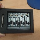 Černý kovový kobylka pro elektrickou kytaru s pěti sedly a pružinami, umístěná v ochranném pěnovém rámu. Na spodní části je vyryt nápis "guyker". Ved…