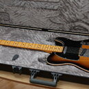 Elektrická kytara typu Telecaster s barevným přechodem korpusu od žluté přes oranžovou k hnědé a černým pickguardem. Nástroj leží v otevřeném tvrdém…