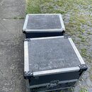 Dvě černé transportní bedny s hliníkovými hranami a kovovými rohy. Na horní části obou beden je bílý nápis MONITOR, přičemž u zadní bedny je text zrc…