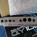 Stříbrný hudební sekvencer s nápisy YAMAHA a QY100. Na zadním panelu jsou umístěny konektory s popisky LINE OUT, PHONES, DC IN, GAIN, GUITAR/MIC INPU…