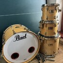 Sada bubnů v přírodním dřevěném provedení. Na basovém bubnu je velký černý nápis Pearl a v dolní části menší nápis Masters, blana má tři červeně lemo…