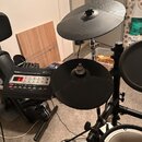 Elektronická bicí souprava s černými gumovými pady a činely. Na ovládacím modulu je nápis Roland TD-3 Percussion Sound Module s displejem a řadou ovl…