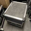 Černý transportní flightcase s hliníkovými hranami a kovovými rohy. Na horní části je bílý nápis "12 MONITOR". Povrch pouzdra vykazuje značné množstv…
