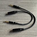Dvě černé audio kabeláže s konektory typu jack na jedné straně a XLR na straně druhé. Na kabelech je viditelný bílý nápis th-mann CE. Povrchy konekto…
