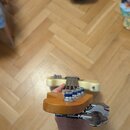 Fotografie zachycuje hlavu elektrické basové kytary z pohledu hráče. Nástroj má dřevěnou barvu a je vybaven čtyřmi stříbrnými ladičkami s modrými pla…