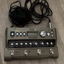 Šedý looper značky LINE 6 s nápisem JM4 Looper. Zařízení má několik ovládacích knoflíků, tlačítka a displej, nad kterým jsou nápisy GUITAR, MIC/AUX,…
