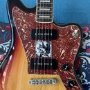 Detail elektrické kytary s tělem v červeno-žlutém sunburst provedení a hnědým hmatníkem. Nástroj má červený perleťový pickguard, dva černá snímače a…