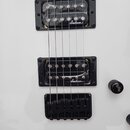 Detail bílé elektrické kytary se dvěma černými humbuckery a černým mostem. Na obou snímačích je bílý nápis Jackson. Povrch kytary vykazuje drobné škr…