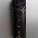 Černý kondenzátorový mikrofon s kovovou mřížkou. Na těle jsou nápisy MUTE, GAIN a HEADPHONES u ovládacích prvků, dále označení KM-2U, logo ve tvaru s…