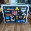 Černý transportní flightcase s hliníkovými hranami a kovovými rohy. Přední strana je polepena různými nálepkami, mezi nimiž jsou nápisy MusicData, be…