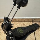 Černý basový pedál s kovovými tyčemi a řetězem. Na šlapce je viditelné logo MAPEX v zelené barvě. Na horním černém knoflíku je nápis 20g. Povrch nást…