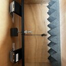 Interiér dřevěné skříně s černým kovovým rámem a šedou akustickou pěnou s pyramidovým profilem. Na rámu jsou upevněny dva černé moduly s kovovými mří…