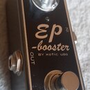 Kompaktní efekt pedál v kovovém stříbrném rámu s černým horním panelem. Na panelu je nápis „EP -booster BY xotic usa“ a vlevo u konektoru označení „O…