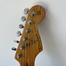 Hlava elektrické kytary z dřeva s viditným opotřebením laku a škrábanci. Na povrchu jsou nápisy „Original Instant Classic“ a „Olden PARTOCASTER WITH…