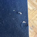 Detailní záběr na tmavě modrý, texturovaný povrch z plsti nebo podobného materiálu. Povrch vykazuje výrazné opotřebení v podobě několika dír a odřeni…