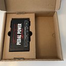 Černý napájecí adaptér Voodoo Lab Pedal Power 2 Plus v hnědé kartonové krabici. Na horní straně je bílý nápis PEDAL POWER a červený nápis 2 PLUS, vle…