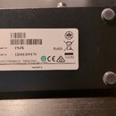 Fotografie zachycuje spodní stranu černého elektronického zařízení s čtyřmi gumovými nožičkami. Uprostřed je bílý štítek s nápisy Model No.: FS3X, Se…