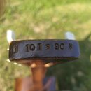Detailní pohled na horní hranu hmatníku nebo hlavy nástroje z tmavého dřeva. Do povrchu je vyryt nápis 1 101 S 90 H. Povrch vykazuje známky opotřeben…
