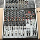 Stříbrný mixážní pult značky behringer s černým šasi. Na horním panelu je nápis 2-TRACK/USB a modelové označení XENYX X1204USB. Zařízení obsahuje něk…