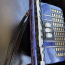 Detailní pohled na modrou akordeon s mramorovaným povrchem. Jsou vidět bílé klávesy, stříbrné kovové mřížky basů a tři bílá ovládací táhla. K nástroj…