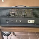 Zadní strana černého kytarového komba s mřížkou, skrze kterou jsou vidět elektronické válvy. Na spodním panelu jsou nápisy F-0.5A, MASTER a PRESENC s…