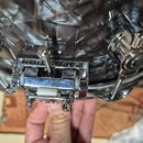 Detailní záběr na chromovaný úchyt s mechanismem u bubnu s černobílým mramorovaným povrchem. Na černé části úchytu je bílý nápis 3P POSITION. Povrchy…