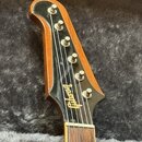 Detail hlavy kytary z dřeva s hnědým lakem a černým plastovým krytem. Na krytu je bílý nápis Gibson v kurzivním písmu a šest stříbrných ladících kolí…