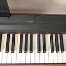 Černý digitální klavír s bílými a černými klávesami. Na horní části korpusu je vlevo nápis DIGITAL PIANO P-115 a vpravo mřížka reproduktoru. Povrch n…