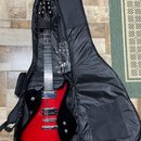 Červená elektrická kytara s tmavým okrajem v černém softcasu. Na hlavě hmatníku je bílý nápis Schecter. Nástroj má dva humbuckery, stříbrný hardware…