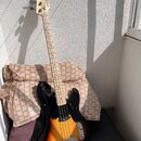 Elektrická basová kytara s tělem v barevném přechodu od žluté přes oranžovou k červené (sunburst) a černým pickguardem. Na hlavě hmatníku je vidět ná…