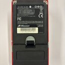 Zadní strana červeného elektronického zařízení s černým plastovým krytem. Na bílém štítku je uveden nápis Maxon, DC INPUT 9V a tabulka s adaptéry AC2…
