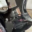 Zadní strana černé elektrické kytary s lesklým povrchem, který vykazuje četné škrábance a známky opotřebení. Na krku je kovová krytka s vyrytym logem…
