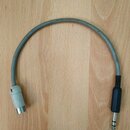 Šedý audio kabel s konektory na obou koncích. Na jedné straně je černý 6,3mm jack konektor a na druhé straně bílý cylindrický konektor s kovovou zako…