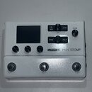 Bílé efektové pedálové zařízení s displejem a třemi stoupacími spínači. Na přední straně je uveden nápis LINE 6 HX STOMP a ovládací prvky s popisky V…
