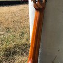 Fotografie zachycuje zadní část krku a hlavy akustické kytary z dřeva s hnědým lakem. Na hlavě jsou vidět bílé ladičky. Nástroj nemá žádné viditelné…