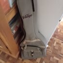 Šedý poloměký pouzdro (gig bag) na hudební nástroj s černým lemováním. V horní části je hnědý nápis v kurzívě Vintage. Pouzdro má v dolní části kapsu…