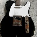 Černá elektrická kytara typu Telecaster s bílým pickguardem a hnedým hmatníkem. Na snímači je viditelný nápis DiMarzio. Instrument vykazuje výrazné o…